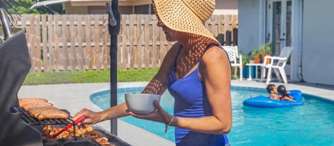 woman barbecuing poolside with kids on float in pool