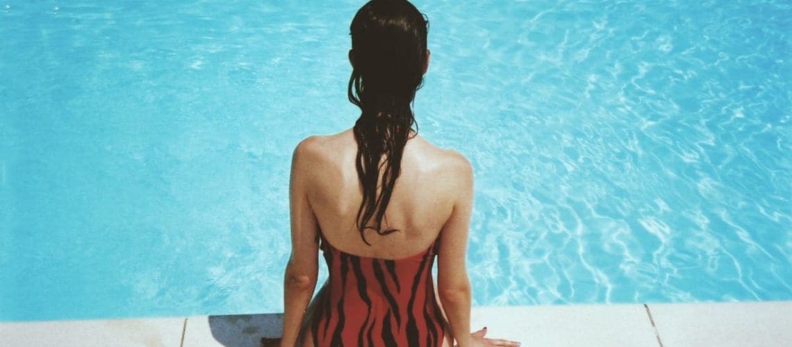 Woman sitting on ledge of pool, concept of knowing the warning signs of a pool in need of pool repair service and care
